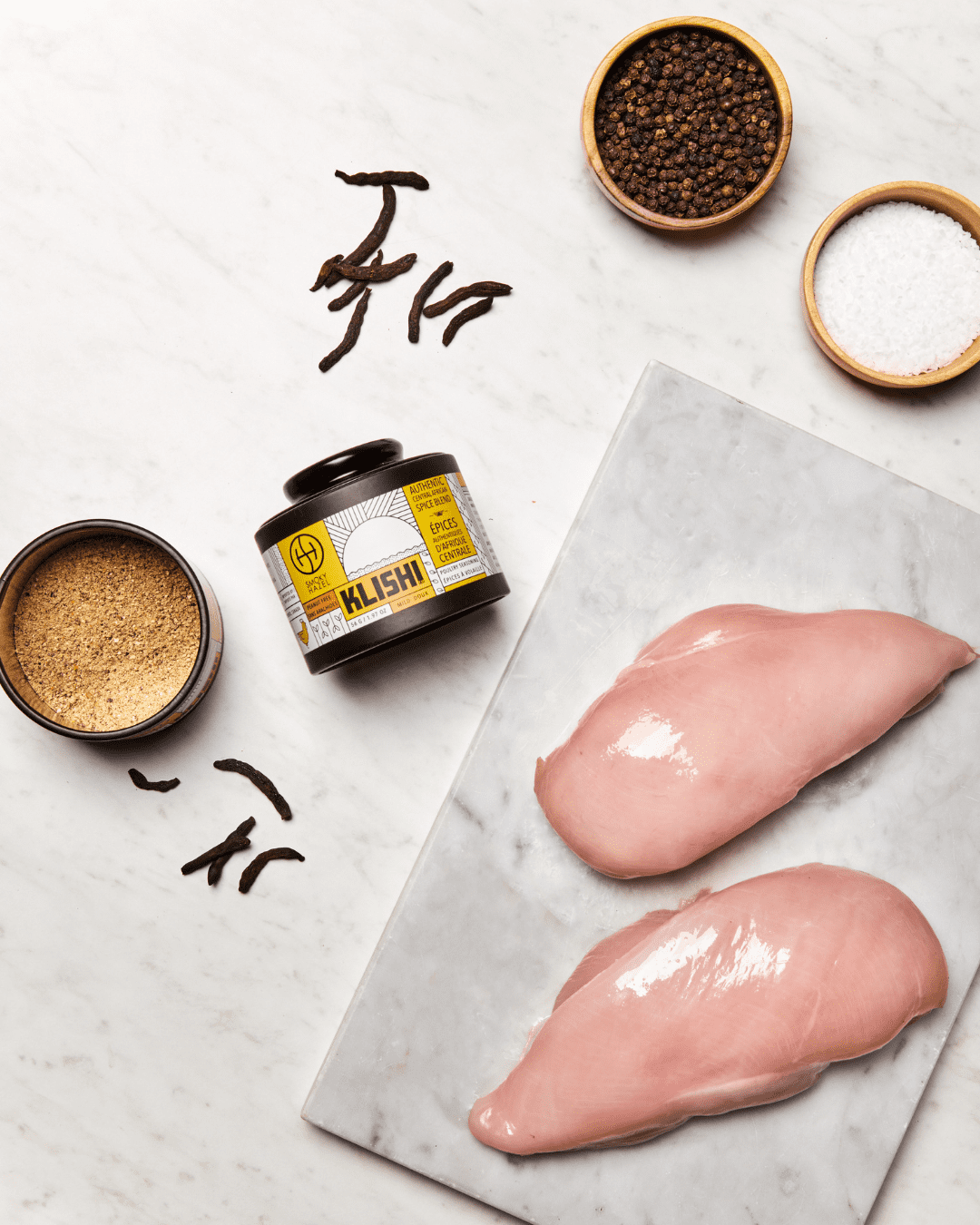Raw chicken breast with klishi spice, peppercorns, salt and selim peppers beside it