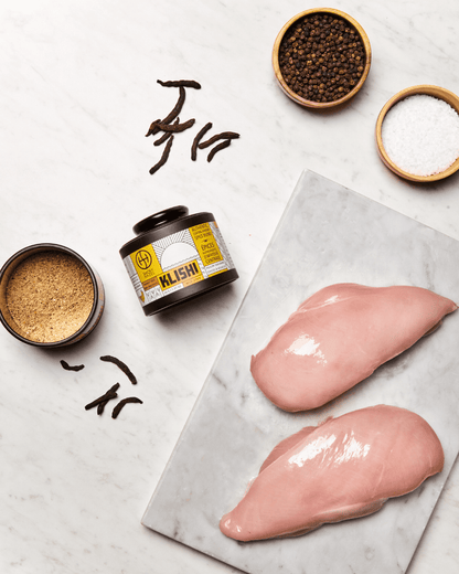 Raw chicken breast with klishi spice, peppercorns, salt and selim peppers beside it